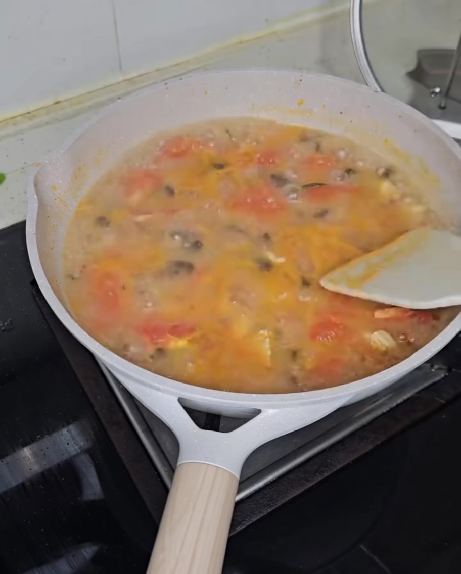 Finely chopped scallions being sprinkled over a pot of steaming tomato chicken dough drop soup.