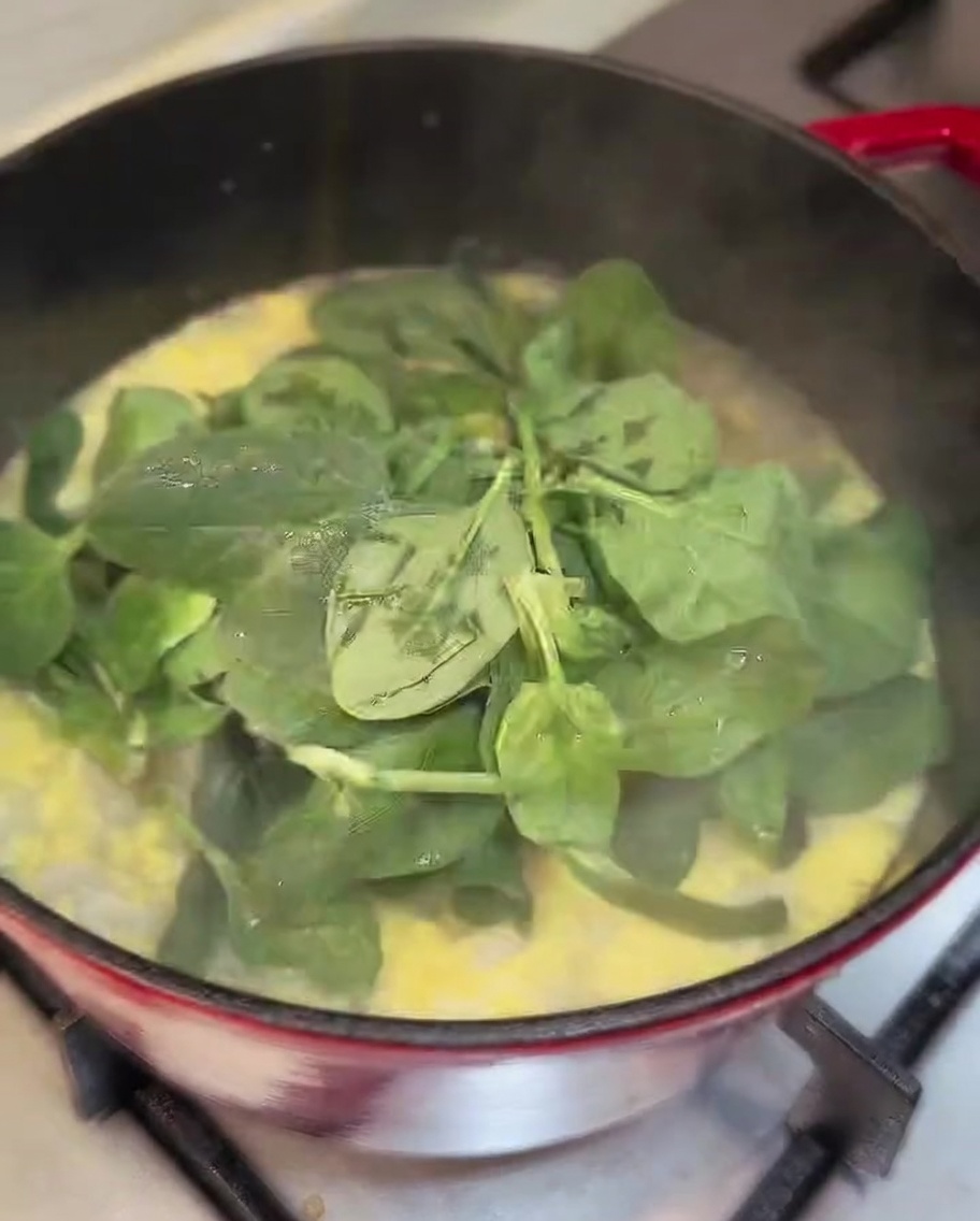 Fresh spinach leaves being stirred into a pot of finished chicken soup.