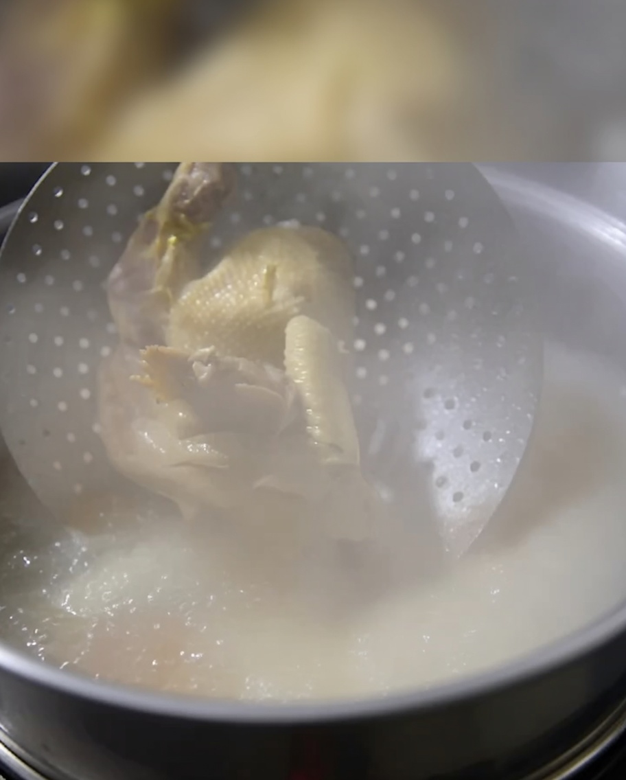 A whole cooked chicken being lowered into a pot of simmering bone broth.