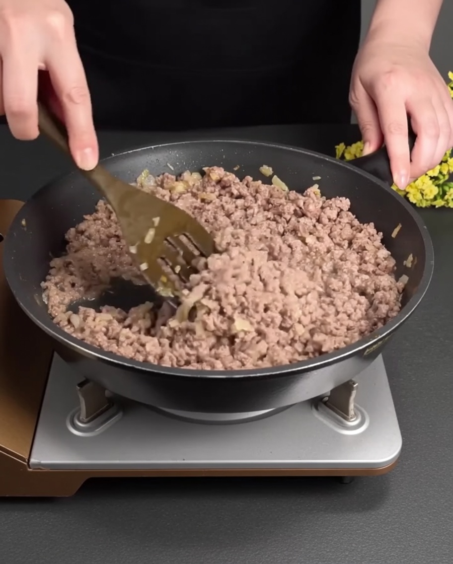 Ground beef browning and breaking apart in a hot pan mixed with softened aromatics.