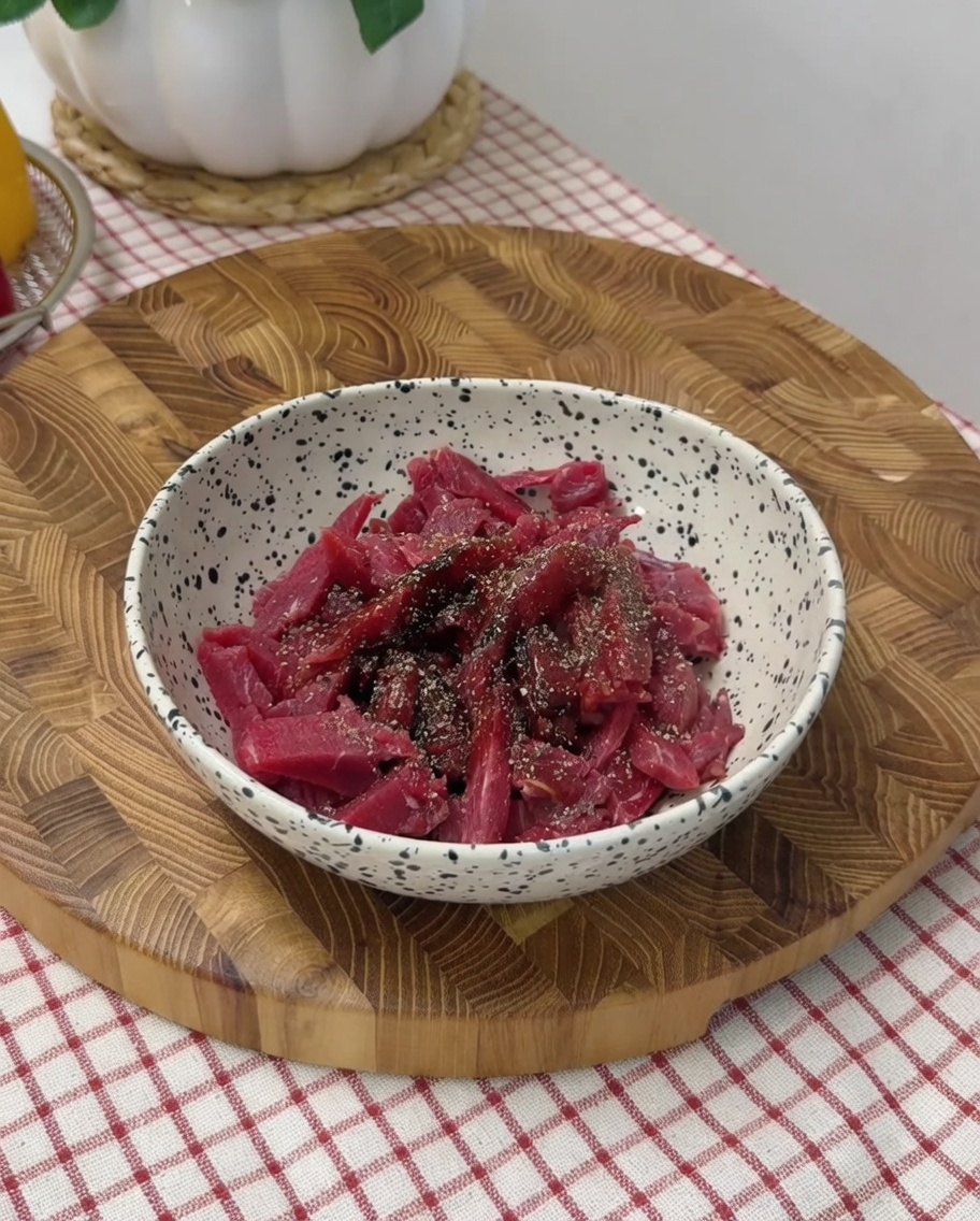 Hand mixing the seasoned beef strips in a mixing bowl.