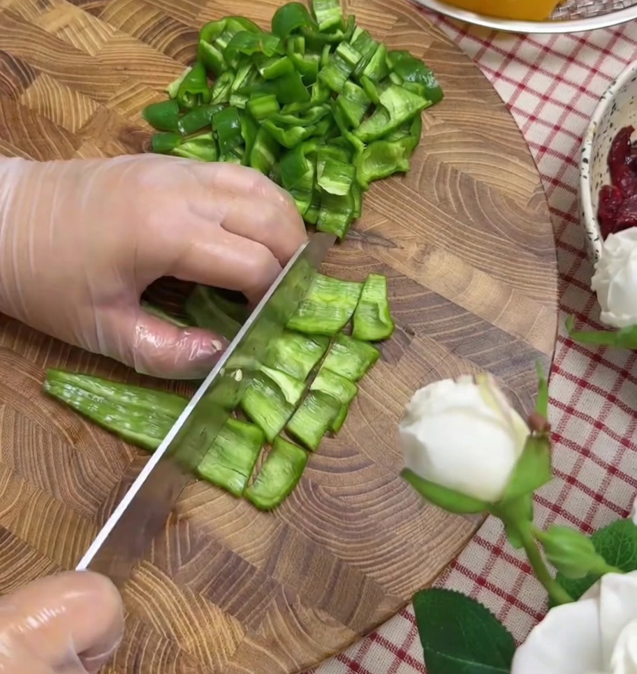 Bell peppers and red onion being chopped into small pieces on a cutting board.