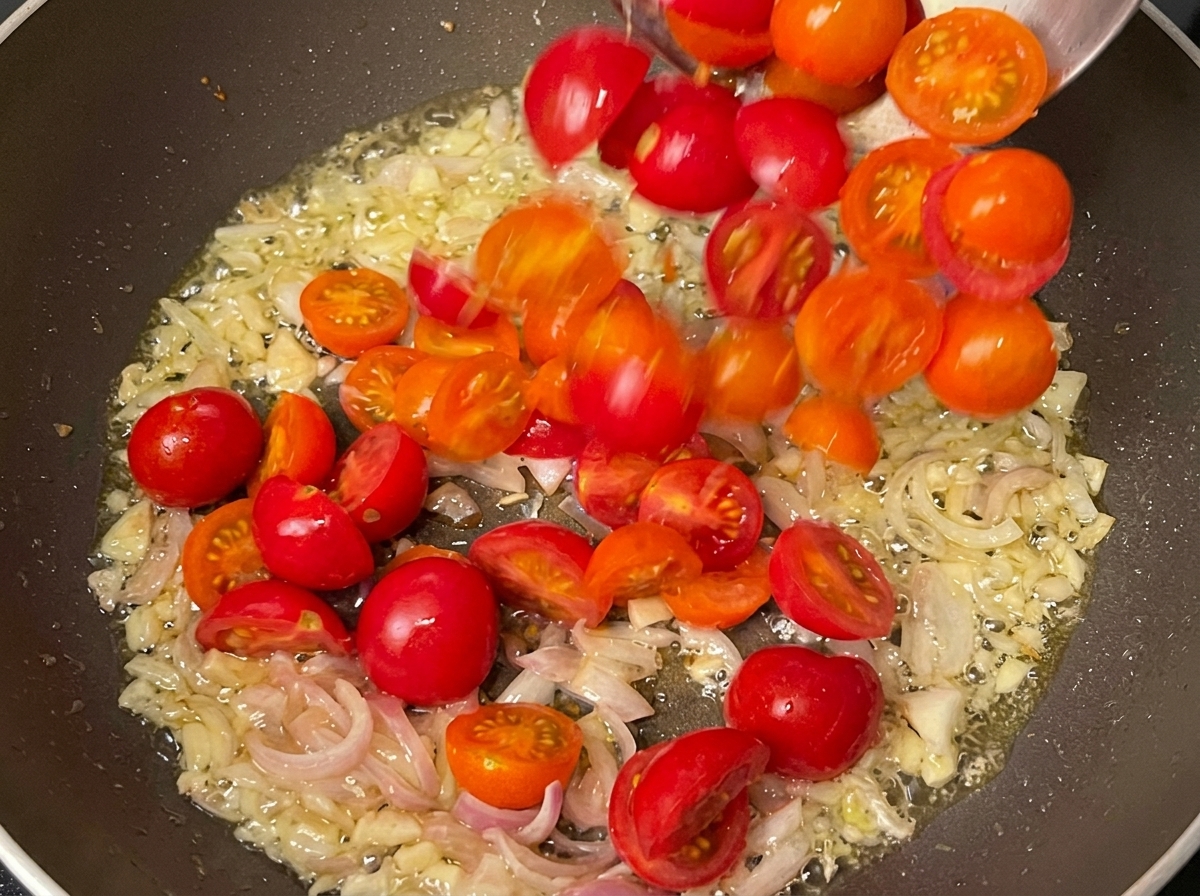 Sautéed aromatics and cherry tomatoes cooking together in a pan.
