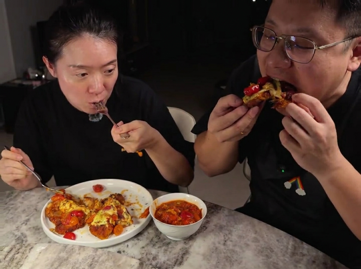 Shredded mozzarella cheese being sprinkled over chicken cutlets covered in tomato sauce in a pan.