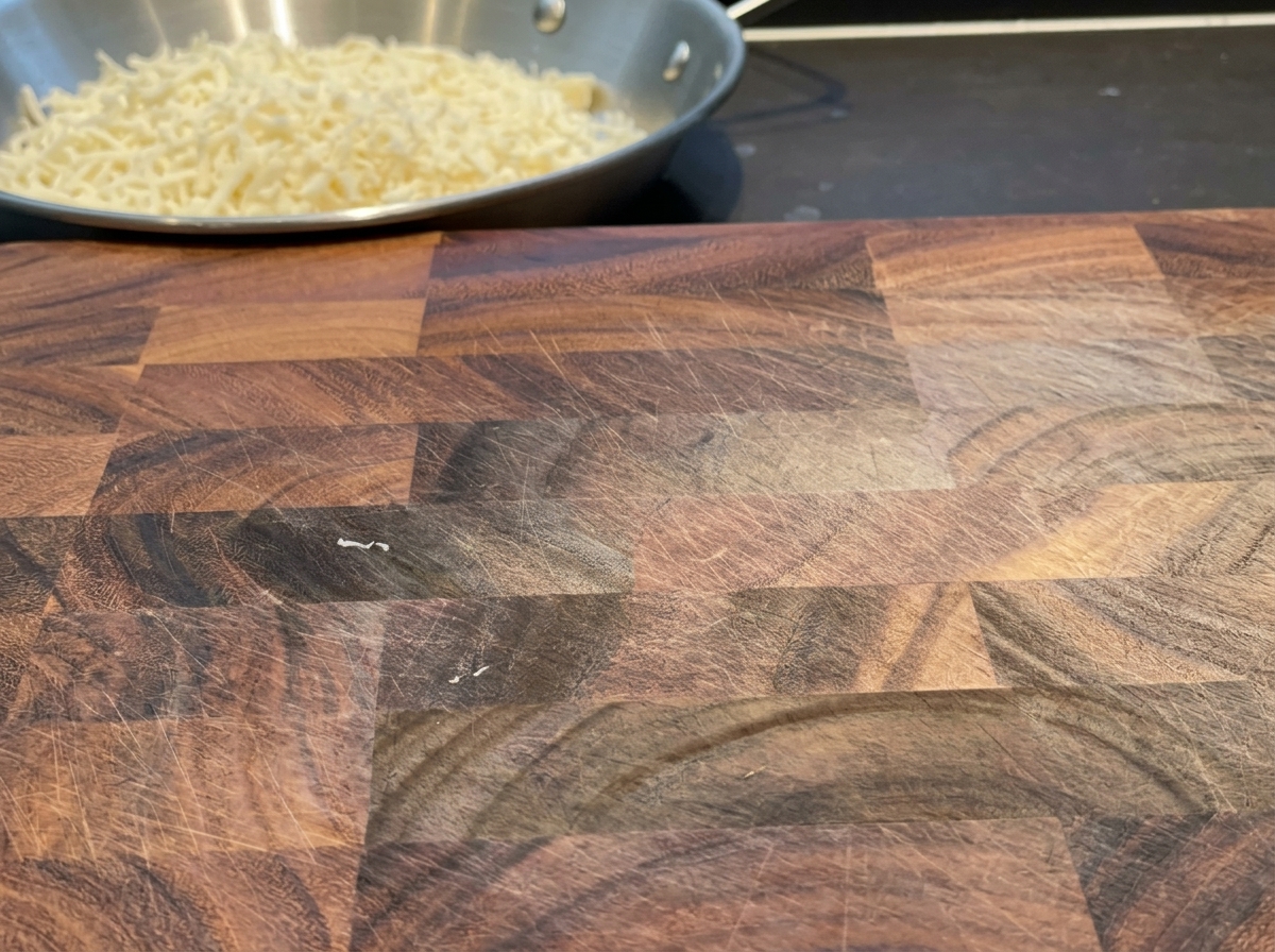 Cheddar cheese slices being cut into uniform strips on a wooden cutting board.