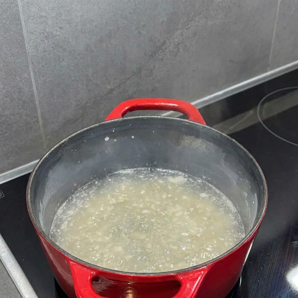 Milk being poured into the roux inside a pot, with a whisk blending them into a smooth liquid.
