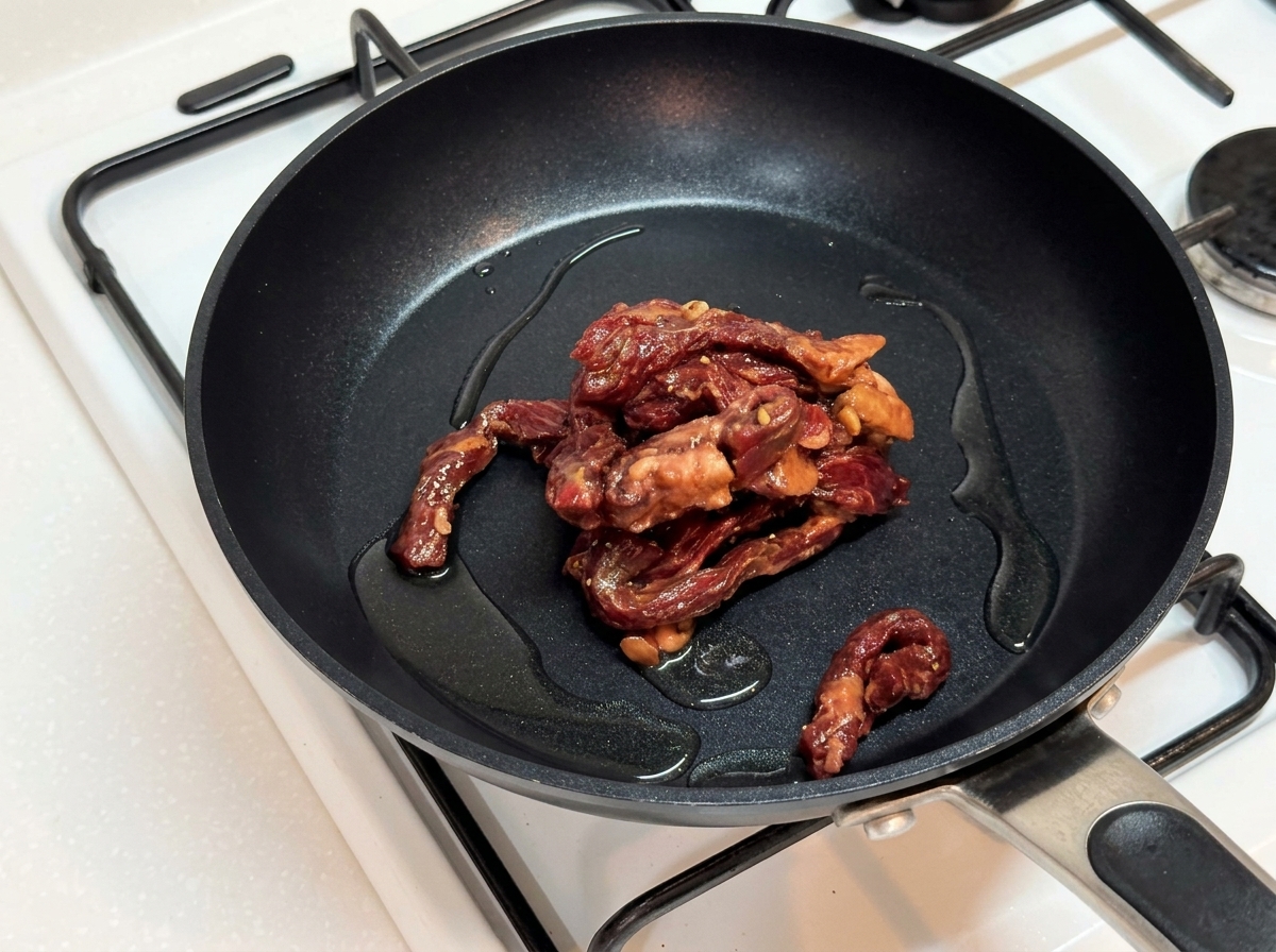 Marinated beef strips browning in a hot, oiled skillet.