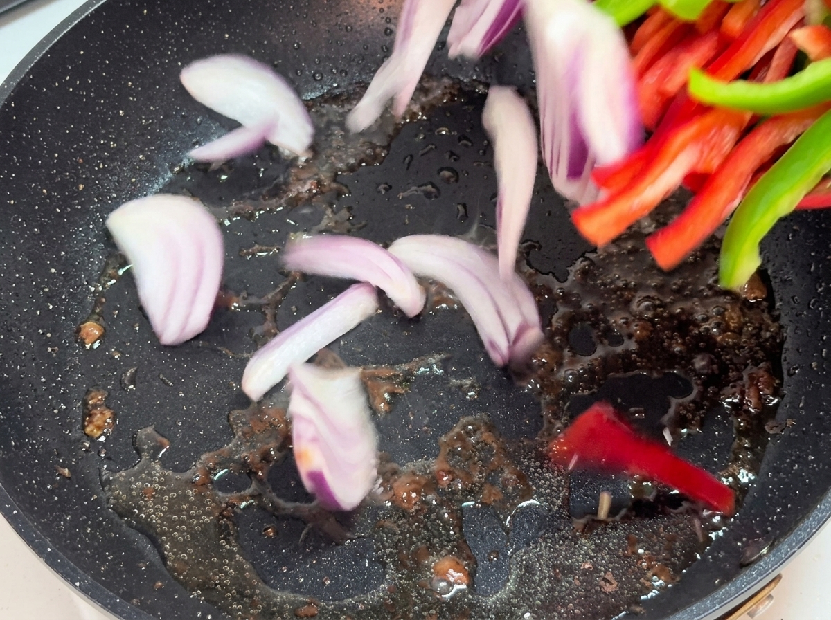 Onion and bell pepper strips sautéing in a hot pan.