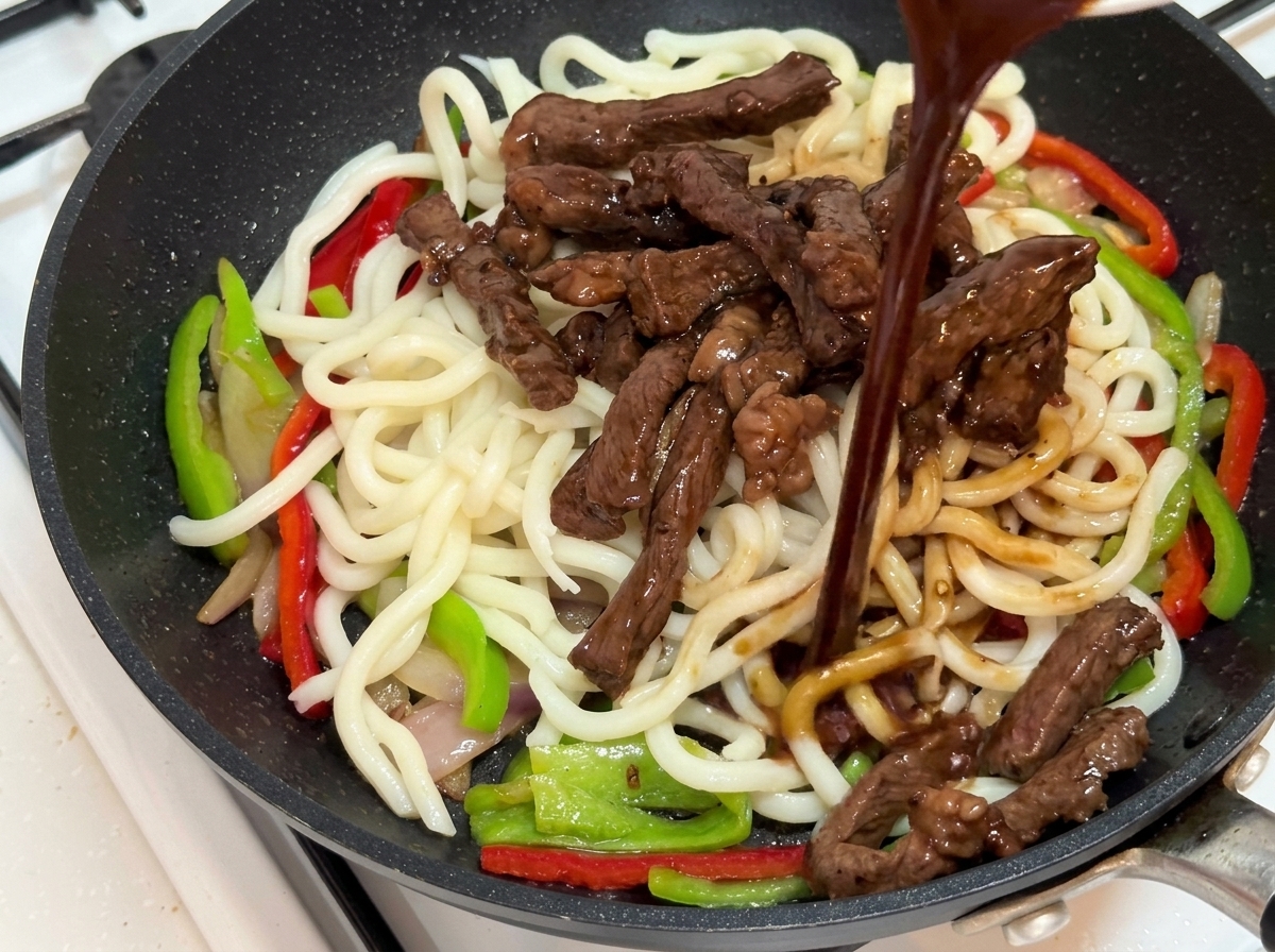 Black pepper sauce being poured over the stir-fry ingredients.