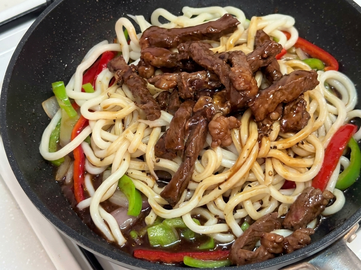 Stir-fry being tossed with tongs in the pan until coated in sauce.