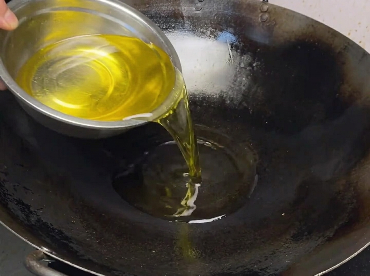 Minced ginger and scallions sizzling in hot oil in a wok, being stirred by a spatula.