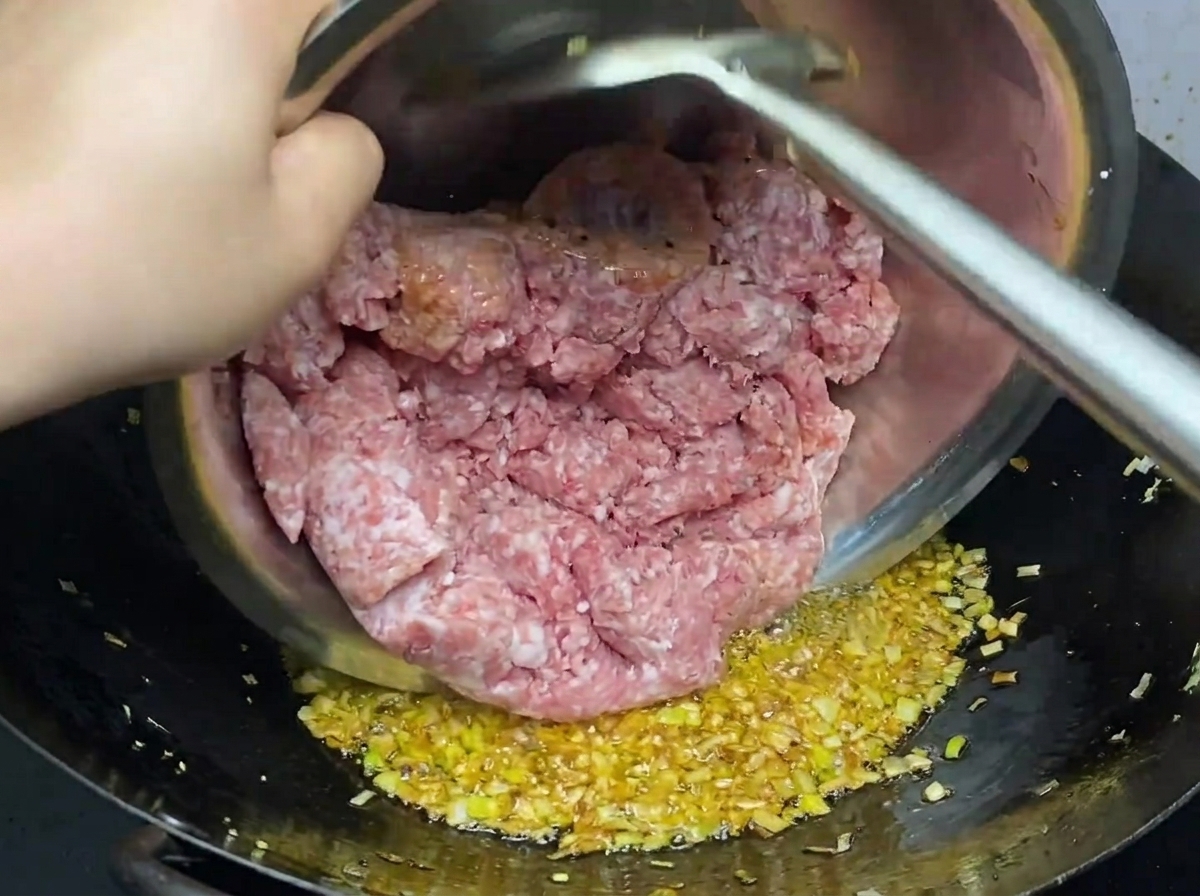 Ground pork being added to the red, spicy oil base in the wok, ready to be broken up and cooked.
