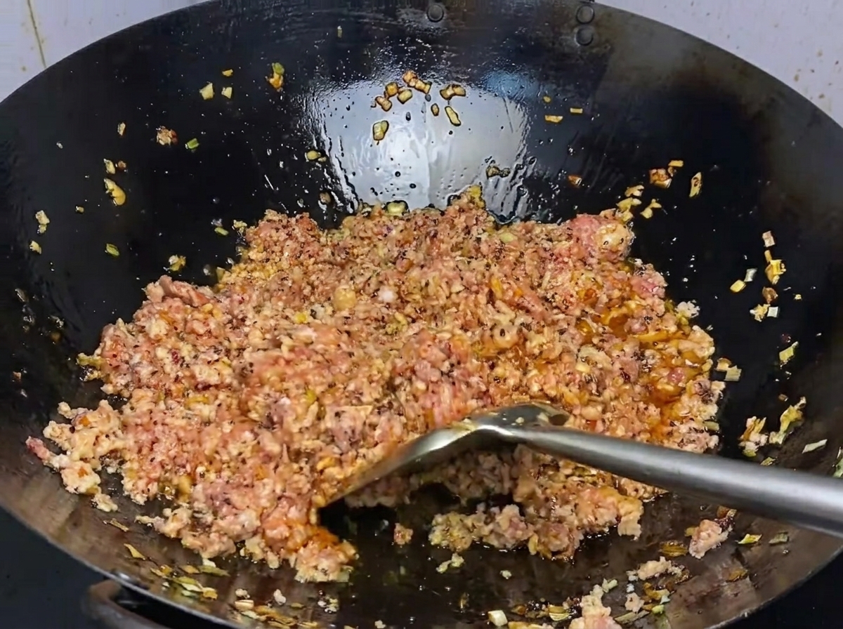 White sugar being sprinkled over the browning pork in the wok.