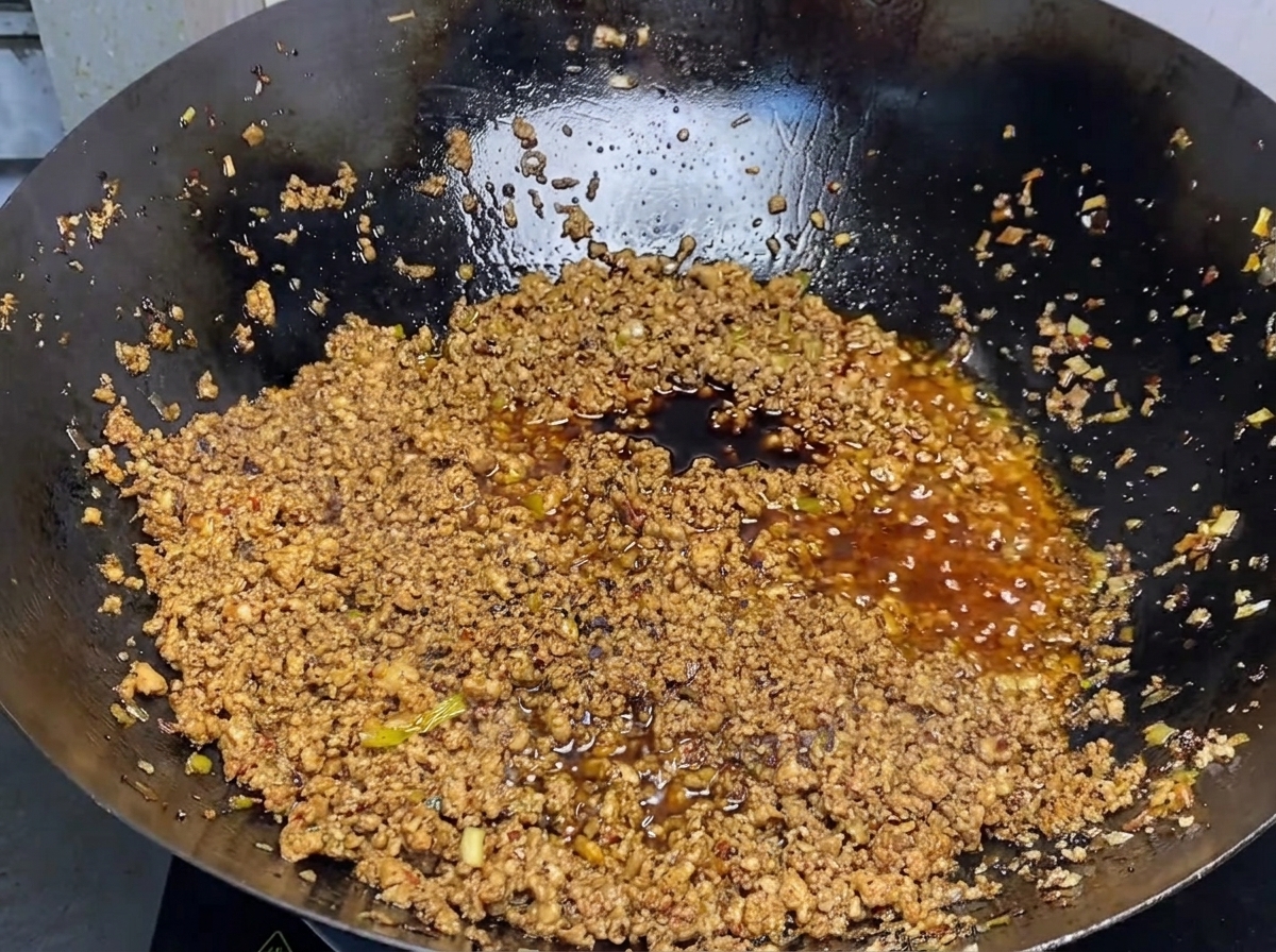 Dark soy sauce being poured into a pan filled with browned ground meat and savory sauce.