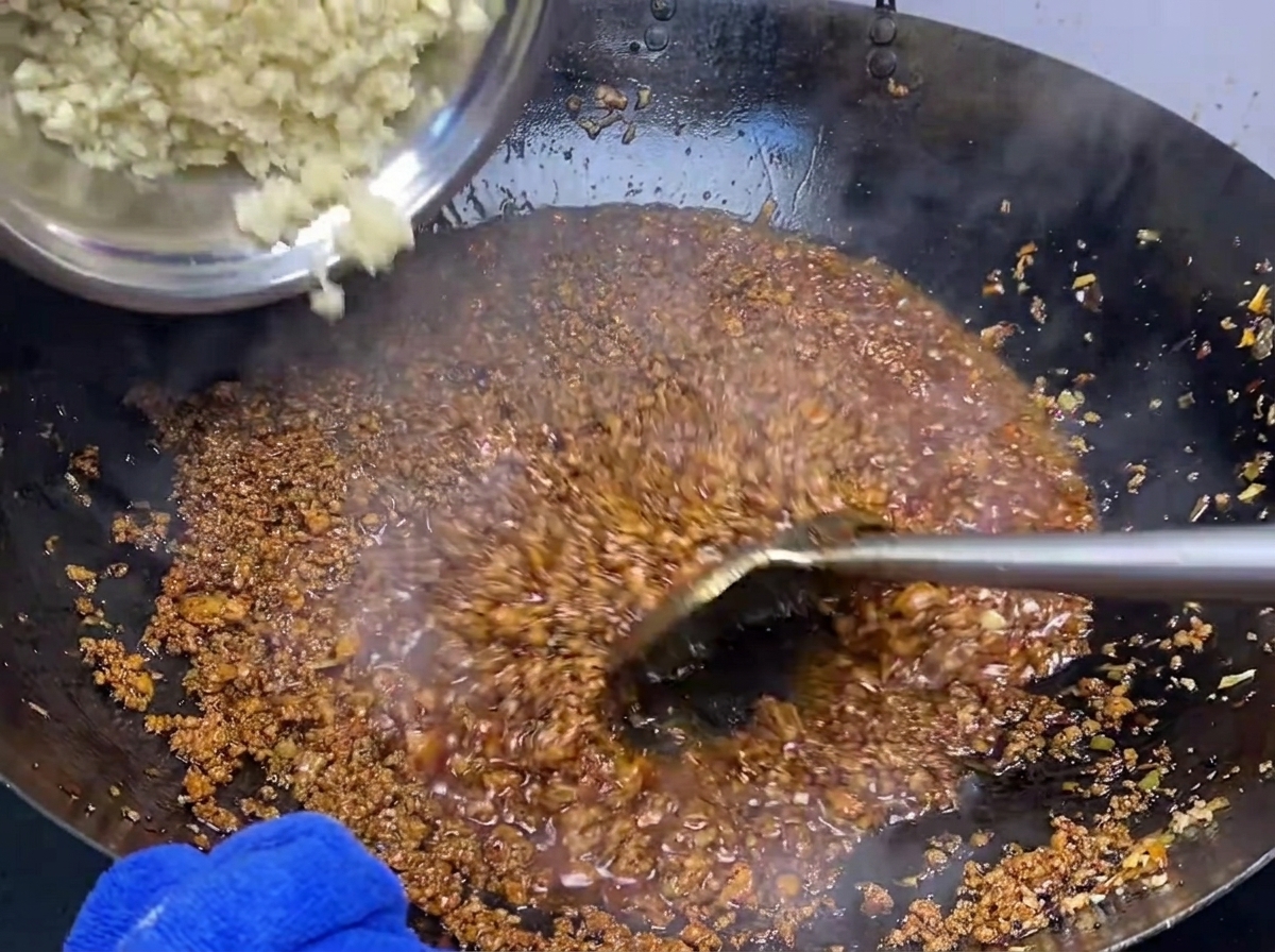 Freshly minced garlic being added to a pan of seasoned ground pork, ready to be stir-fried.