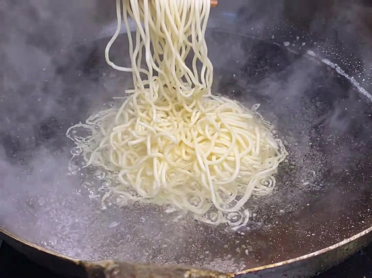 Fresh noodles being lowered into a large pot of boiling water.