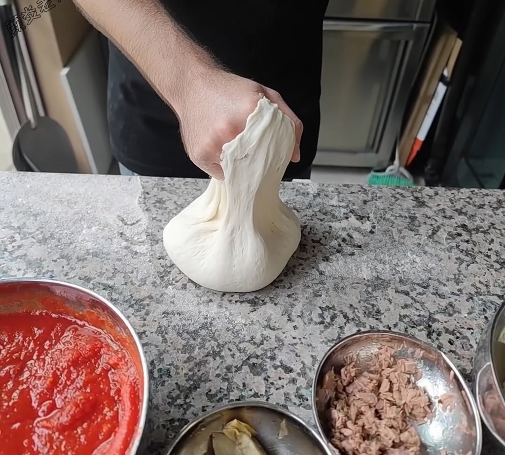Chef stretching the pizza dough by rotating it over his knuckles to achieve the desired diameter.