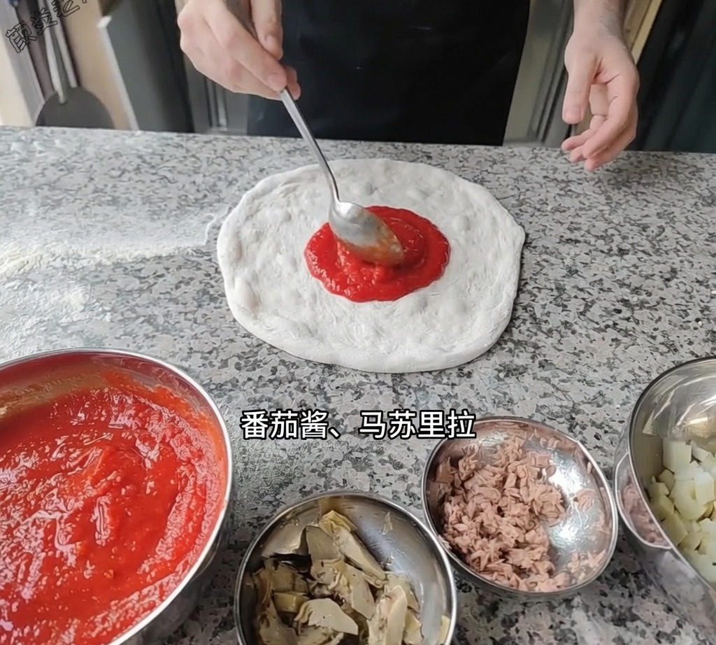 A ladle spreading smooth red tomato sauce over the pizza dough base on the work surface.