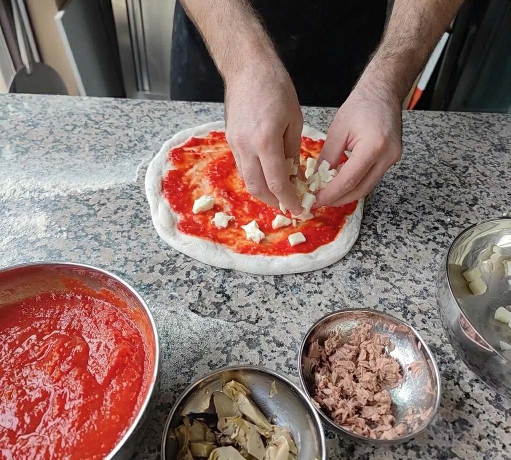 Small cubes of fresh white mozzarella cheese being scattered onto the tomato sauce base.