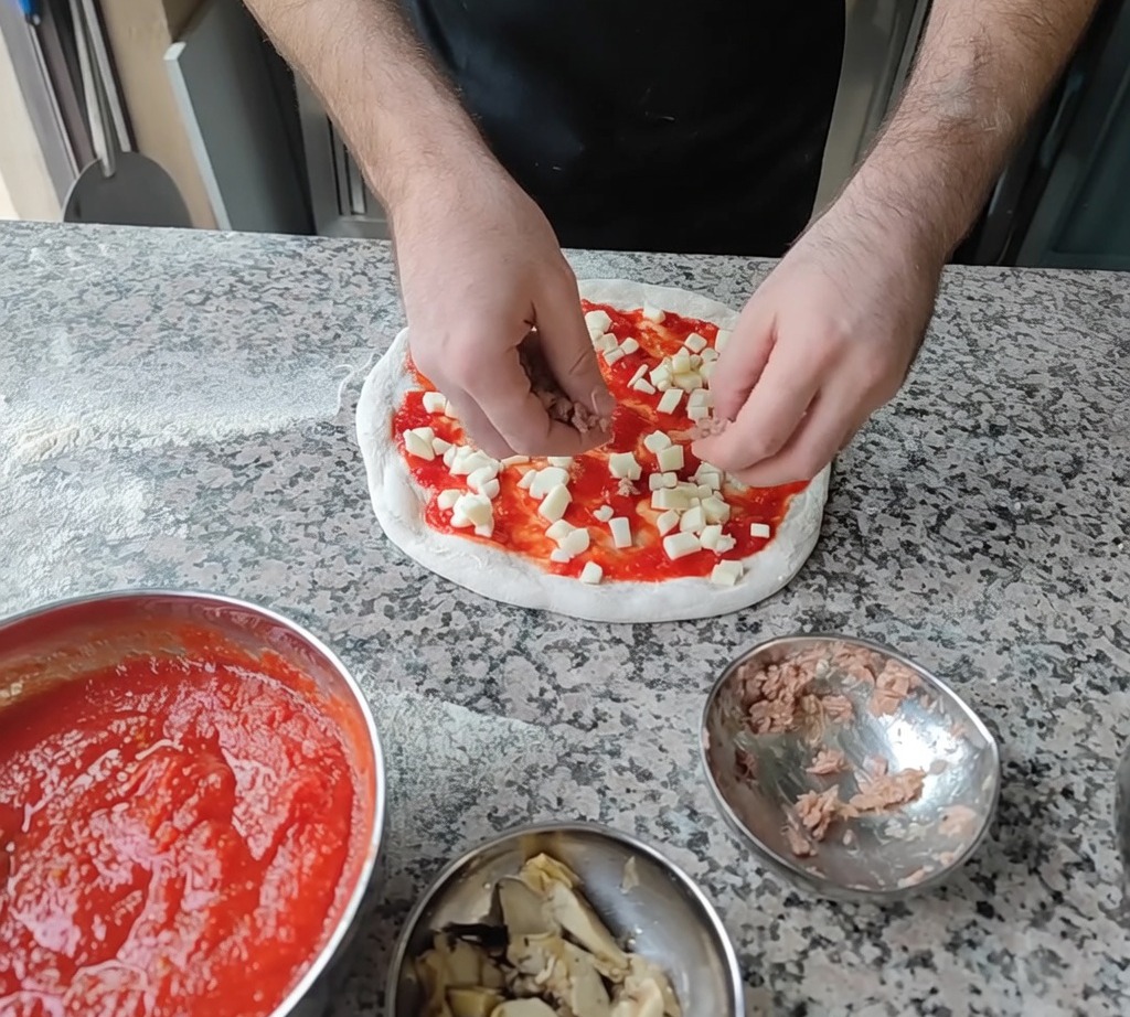 Adding tuna flakes and artichoke slices onto the pizza as final toppings.