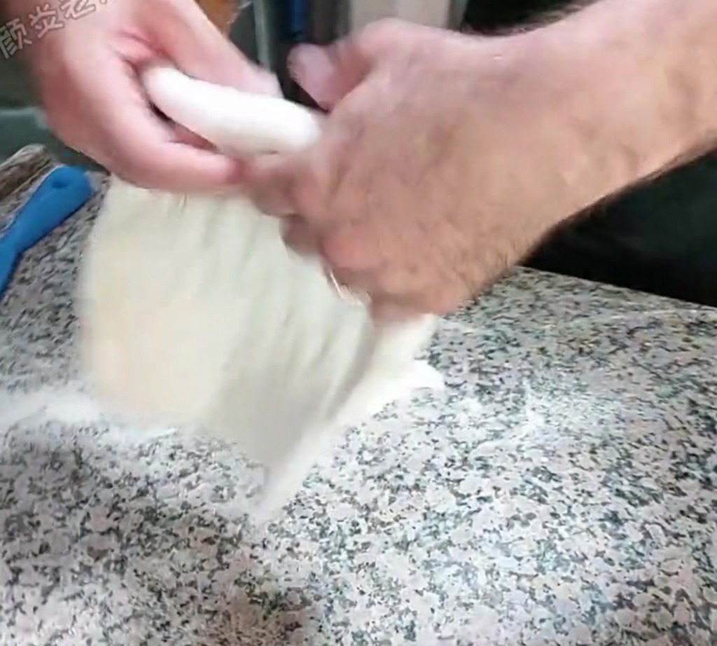 Dough being stretched by hand using a slapping technique on a floured countertop.
