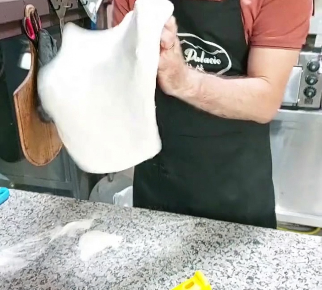A pizza dough base being shaped by tossing it in the air.