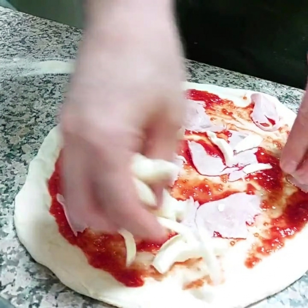 Chunks of mozzarella cheese being added to the pizza base.