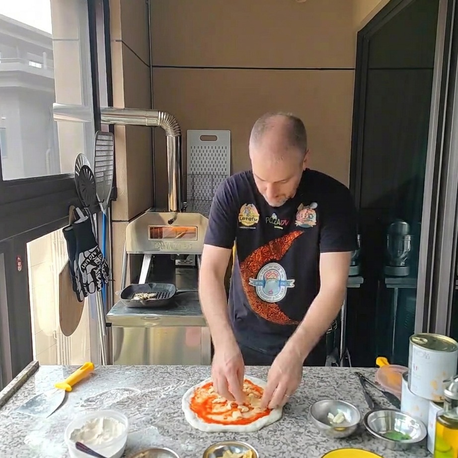 Shredded mozzarella cheese being sprinkled over the tomato-sauced pizza dough.