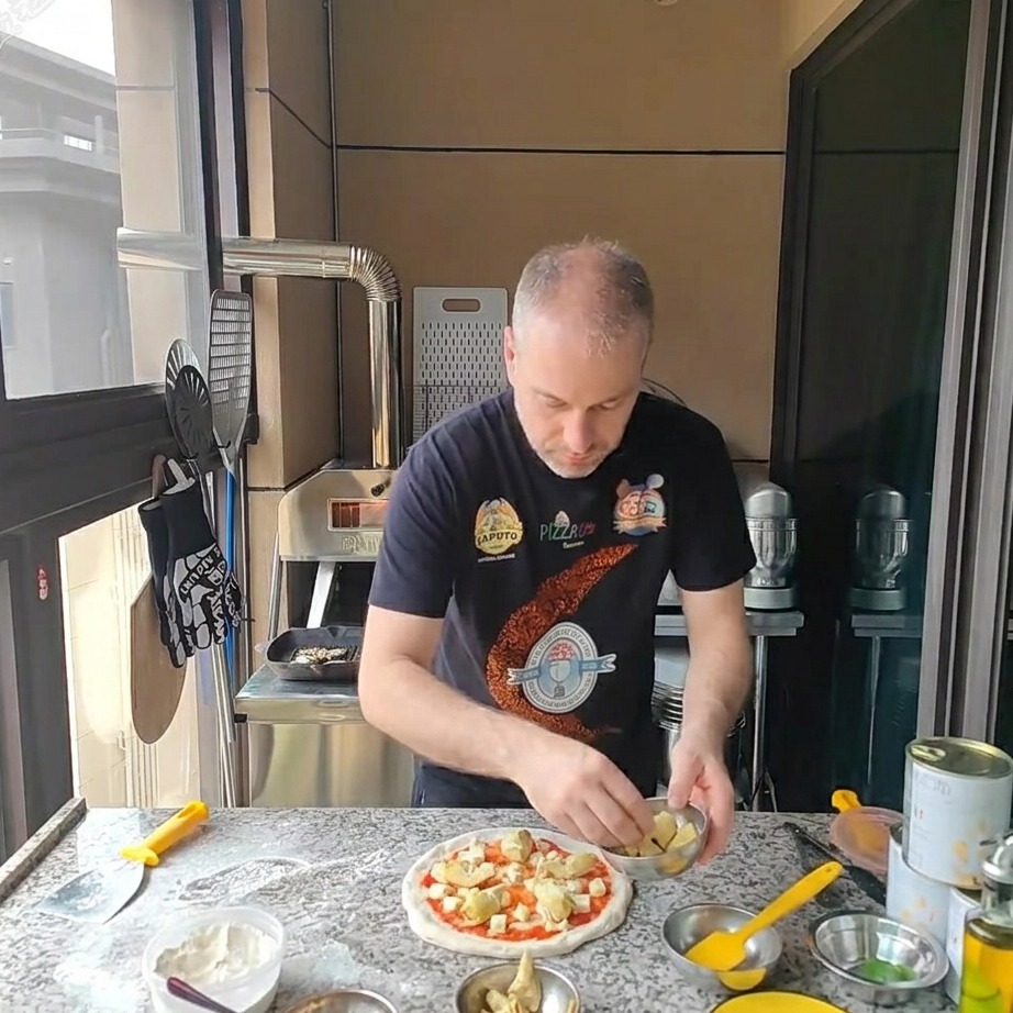 Pieces of canned artichoke hearts being placed on the cheese-covered pizza.