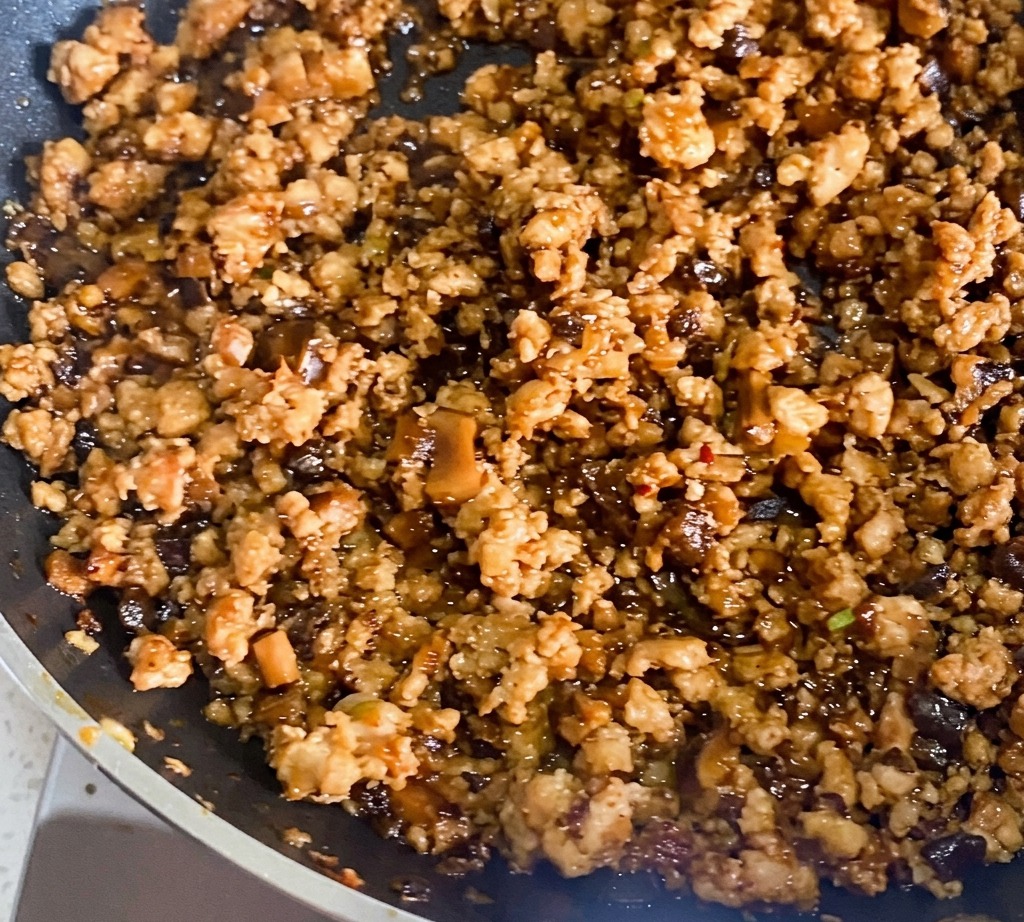 Close-up of minced meat being stir-fried in a dark, seasoned oil until browned.