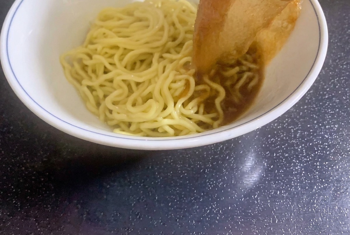 Freshly cooked curly ramen noodles being placed into a serving bowl.