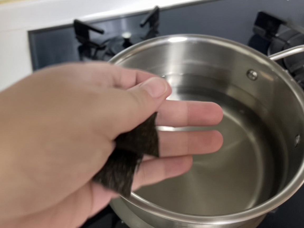 Two pieces of kelp being submerged into a pot of fresh, cold water.