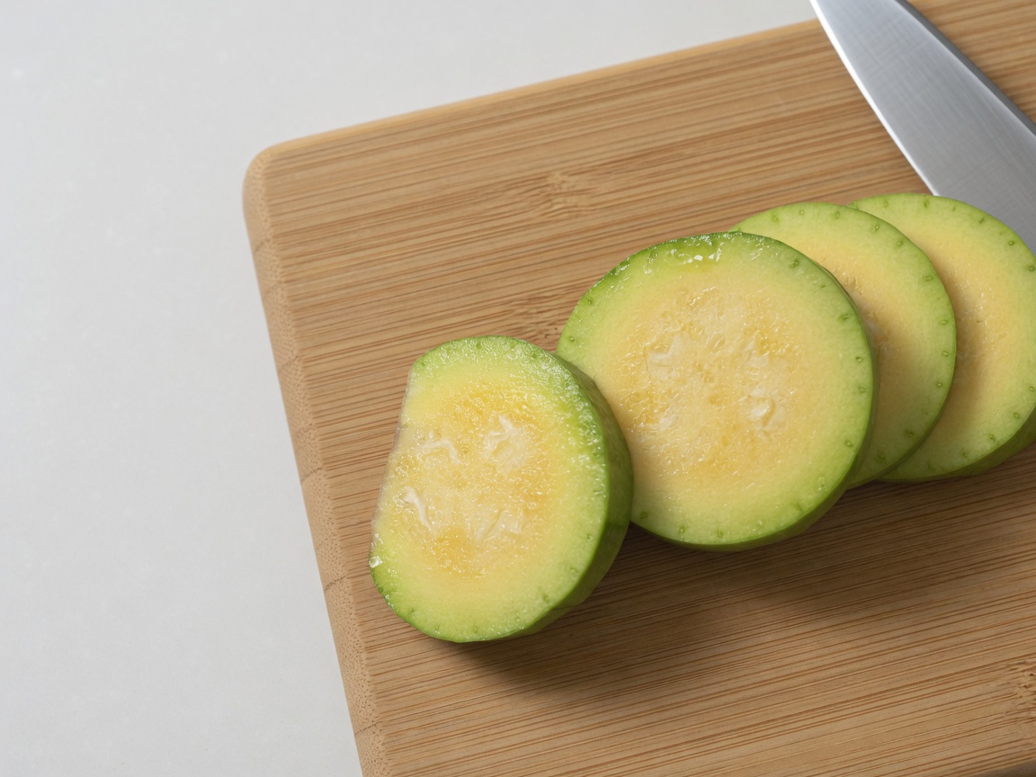 A sharp knife slicing through a fresh green zucchini on a wooden board.