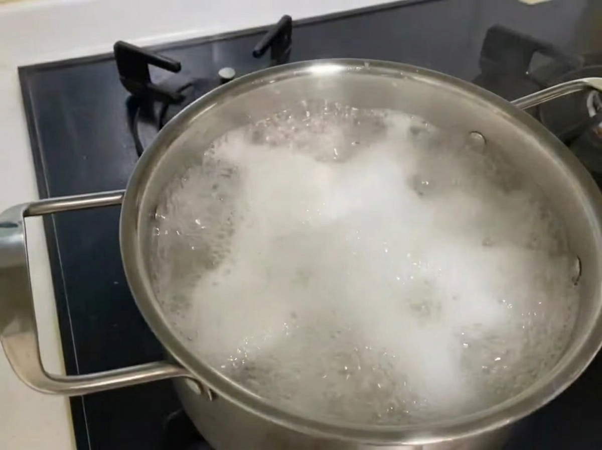 Green zucchini strips being poured into a pot containing boiling noodles and clams.