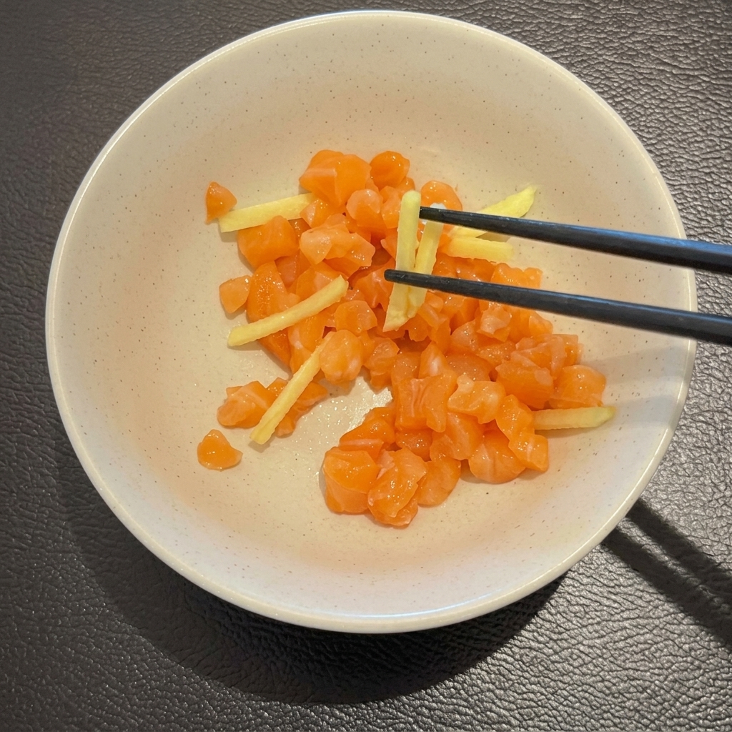Diced raw salmon and julienned ginger being mixed with chopsticks in a white bowl.