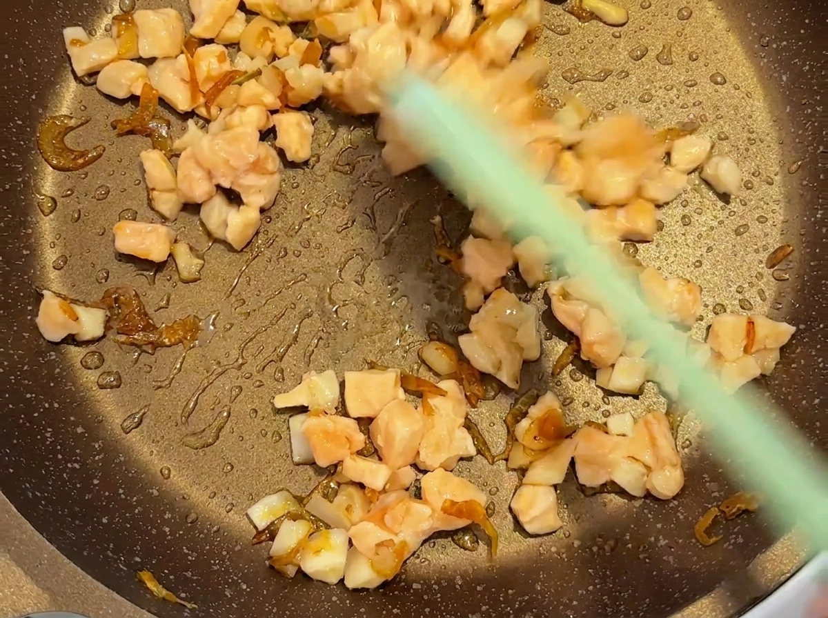 A green spatula stirring diced salmon and dried shrimp in a heated pan