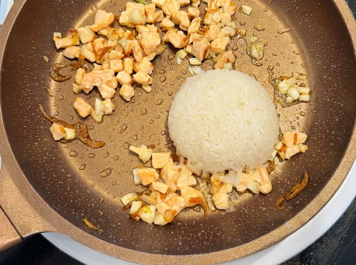 A scoop of washed raw white rice and diced raw salmon placed in a pan alongside the sauteed shrimp mixture