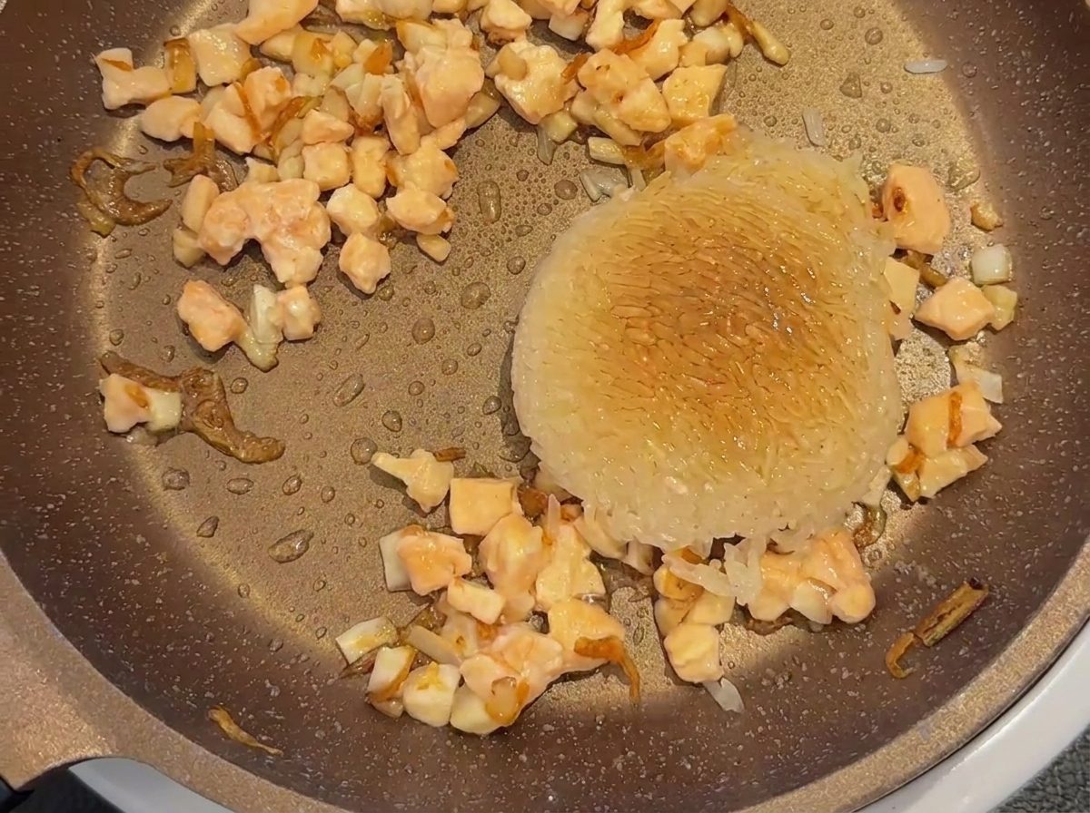 Baby soy sauce sprayed over a scoop of white rice and diced salmon in a pan.