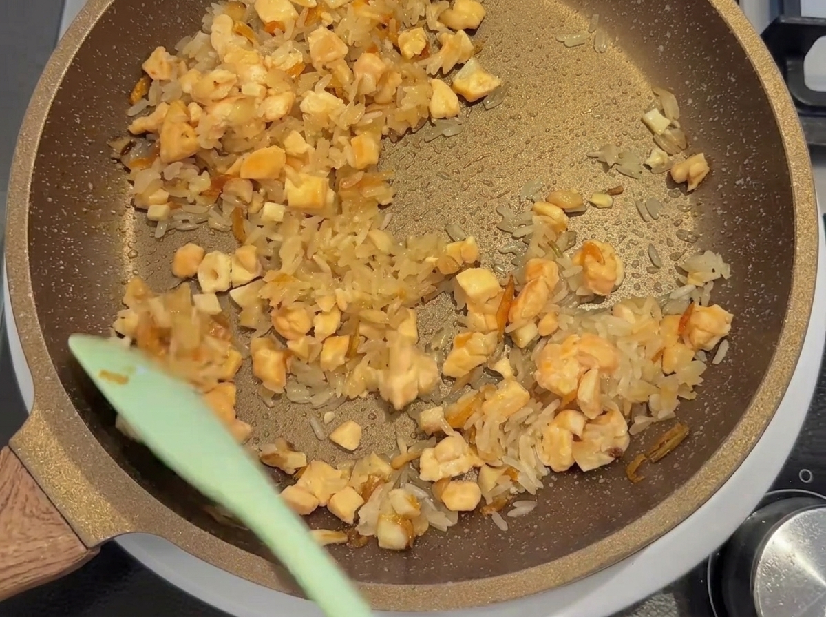 White rice, diced salmon, and other ingredients being stir-fried together in a pan.
