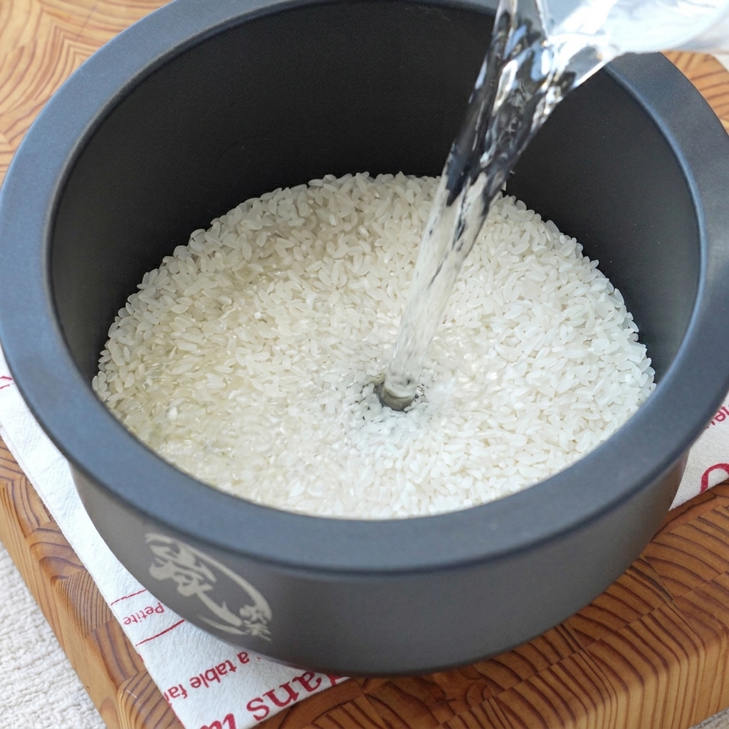 Fresh water being poured into the rice cooker pot over raw white rice grains.