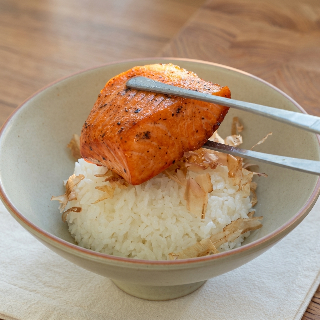 A golden-brown pan-seared salmon fillet being placed with tongs onto a mound of white rice.