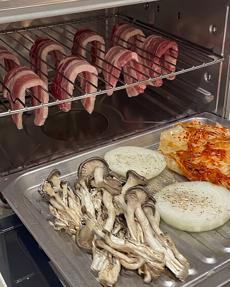 Baking tray with vegetables and kimchi positioned underneath the hanging pork belly in the oven.