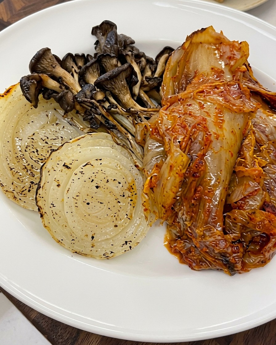 Sesame seeds being sprinkled over the top of the roasted vegetables and kimchi on a plate.