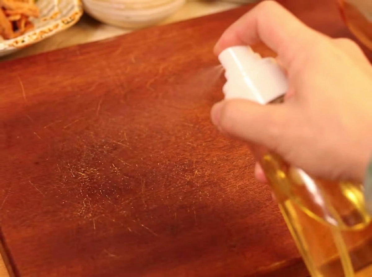 A hand using a spray bottle to lightly oil mushrooms arranged on a baking sheet.