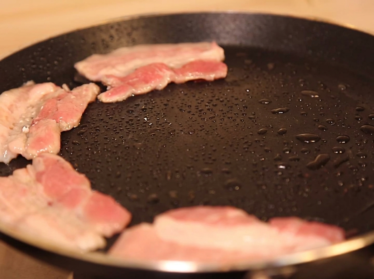 Pork belly slices cooking in a hot pan with a small amount of oil, beginning to brown.