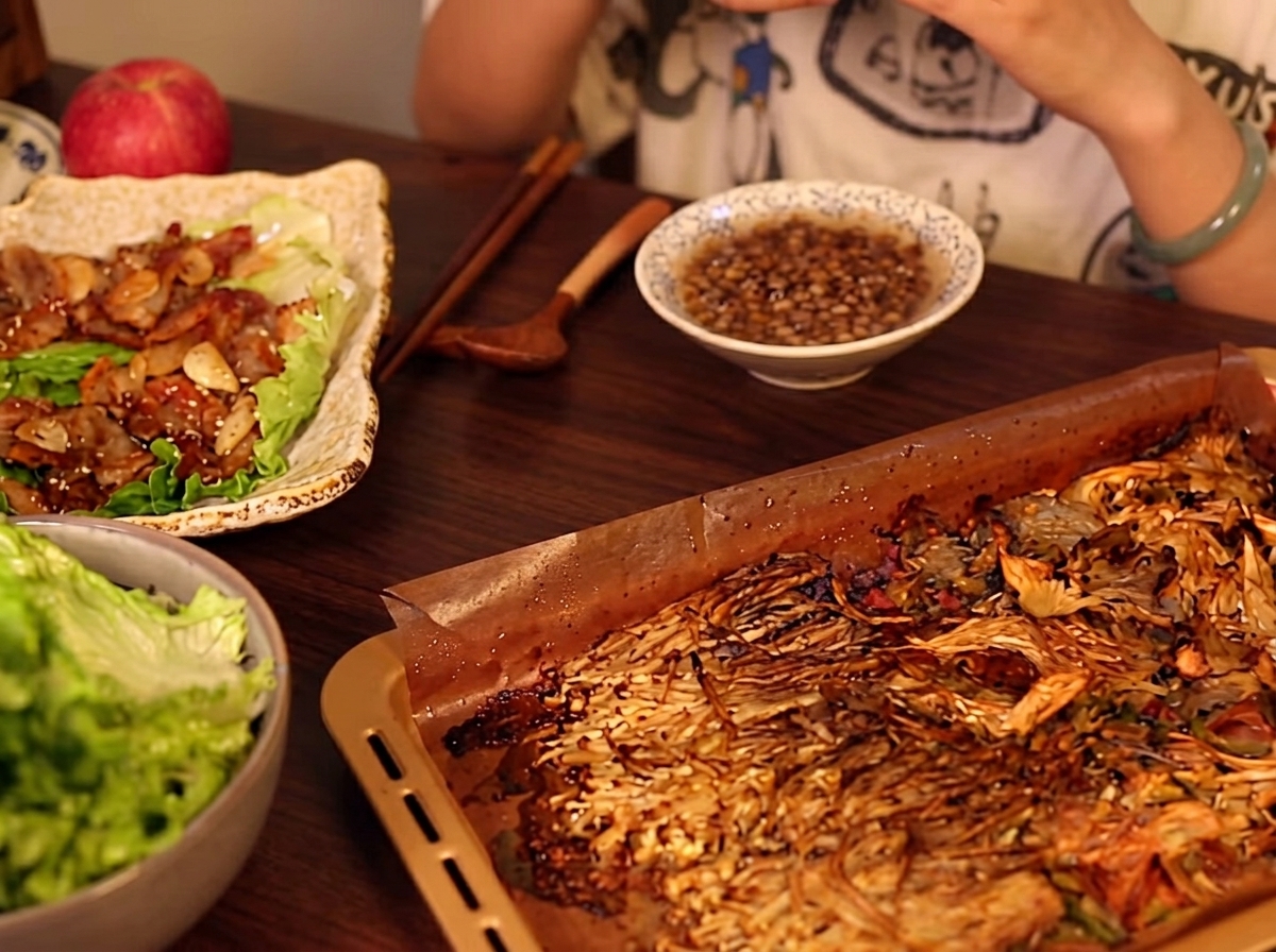 White pepper, cumin, and white sesame seeds being sprinkled over the cooked pork belly in the pan.