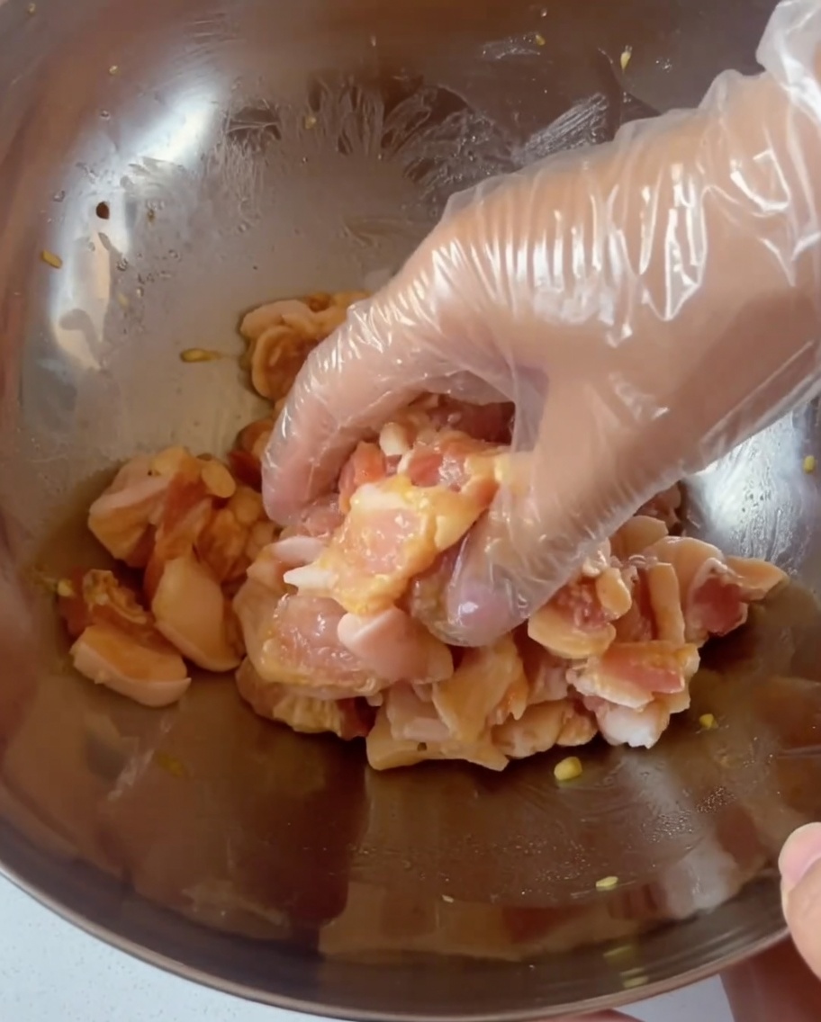 A gloved hand mixing seasoned pork belly slices in a large stainless steel bowl.
