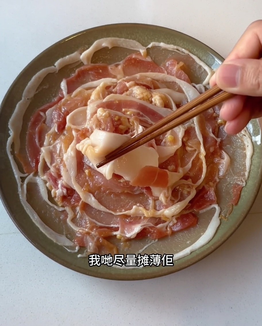 Marinated pork belly slices being carefully spread out in a single layer on a plate using chopsticks.
