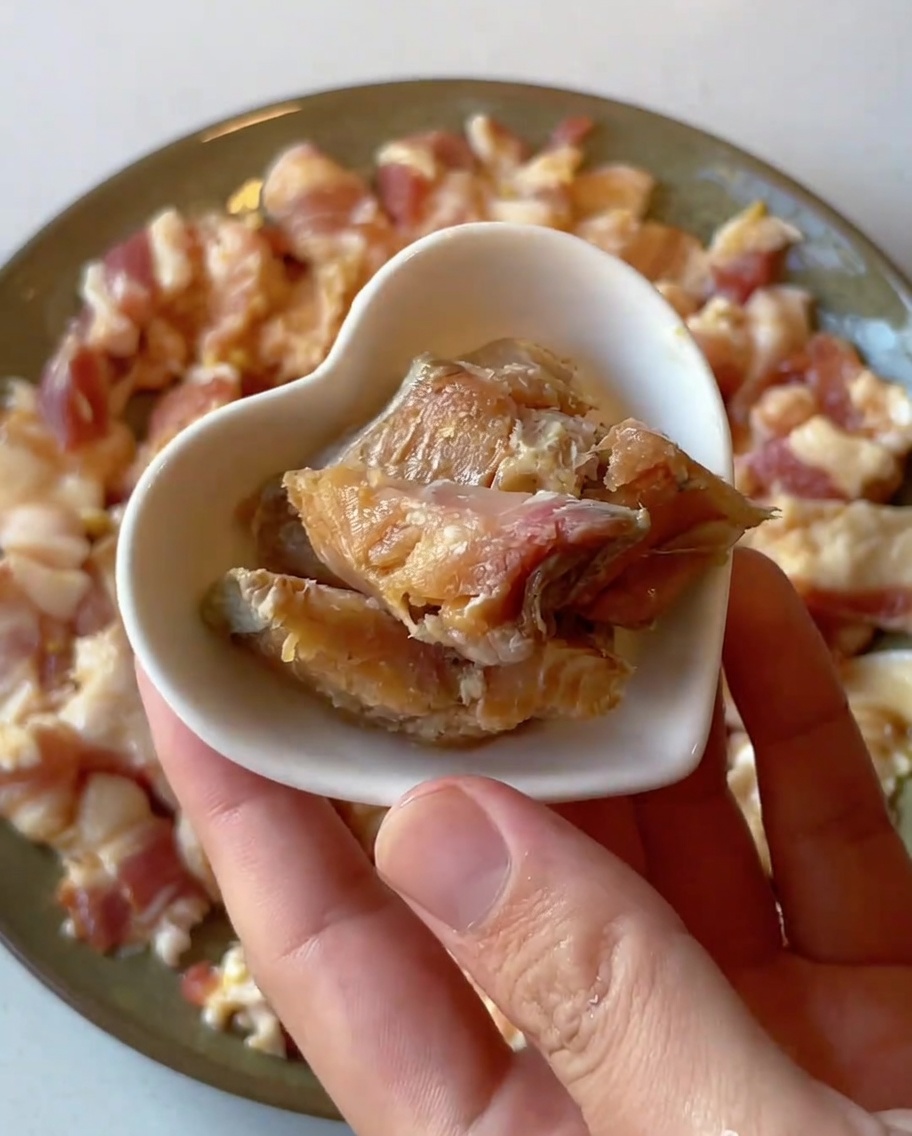 Close-up of small pieces of preserved salted fish being placed onto a plate of raw marinated pork.