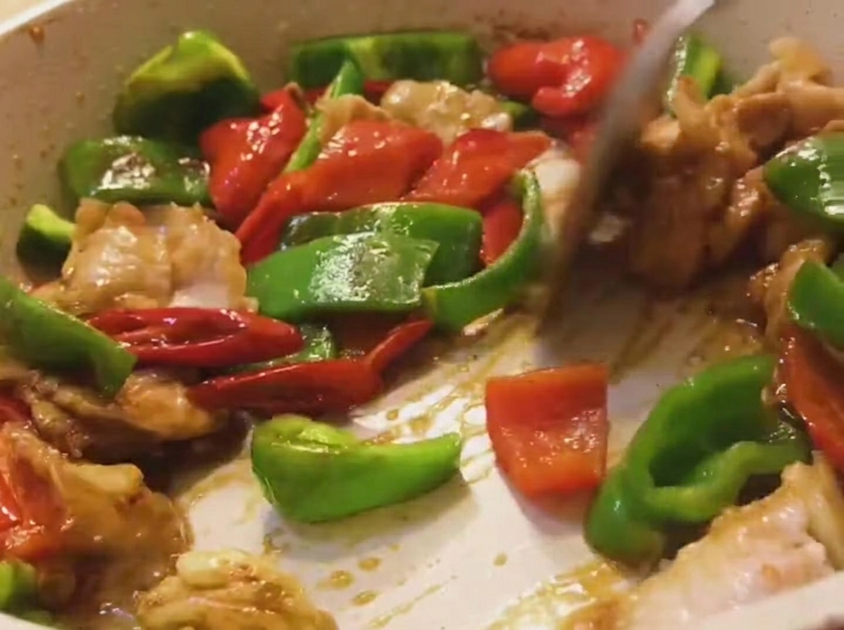 A mixture of pork, green bell peppers, and red bell peppers being tossed in a pan with a wooden spatula.